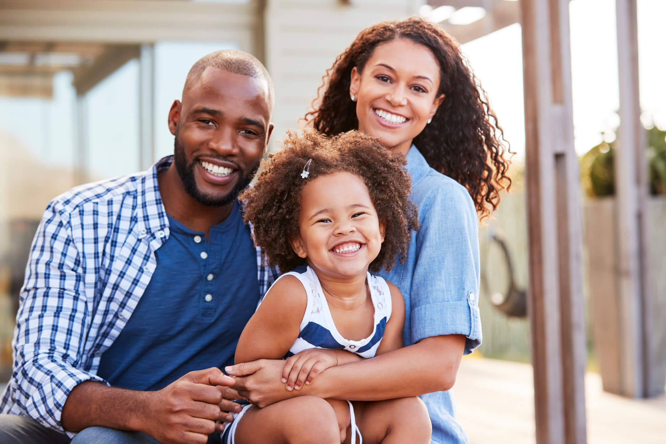 A family of three embracing outdoors and smiling at camera.